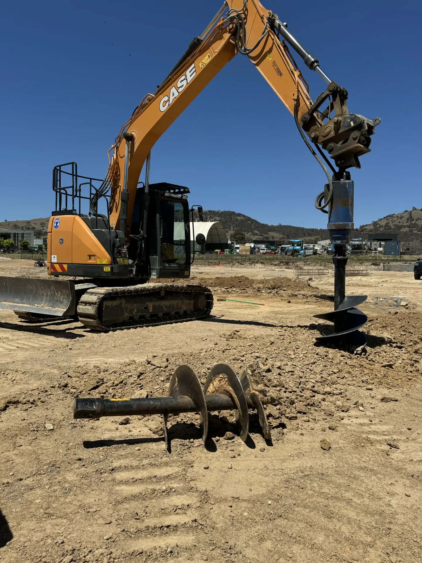 Excavator auger drilling a post hole in a dirt yard