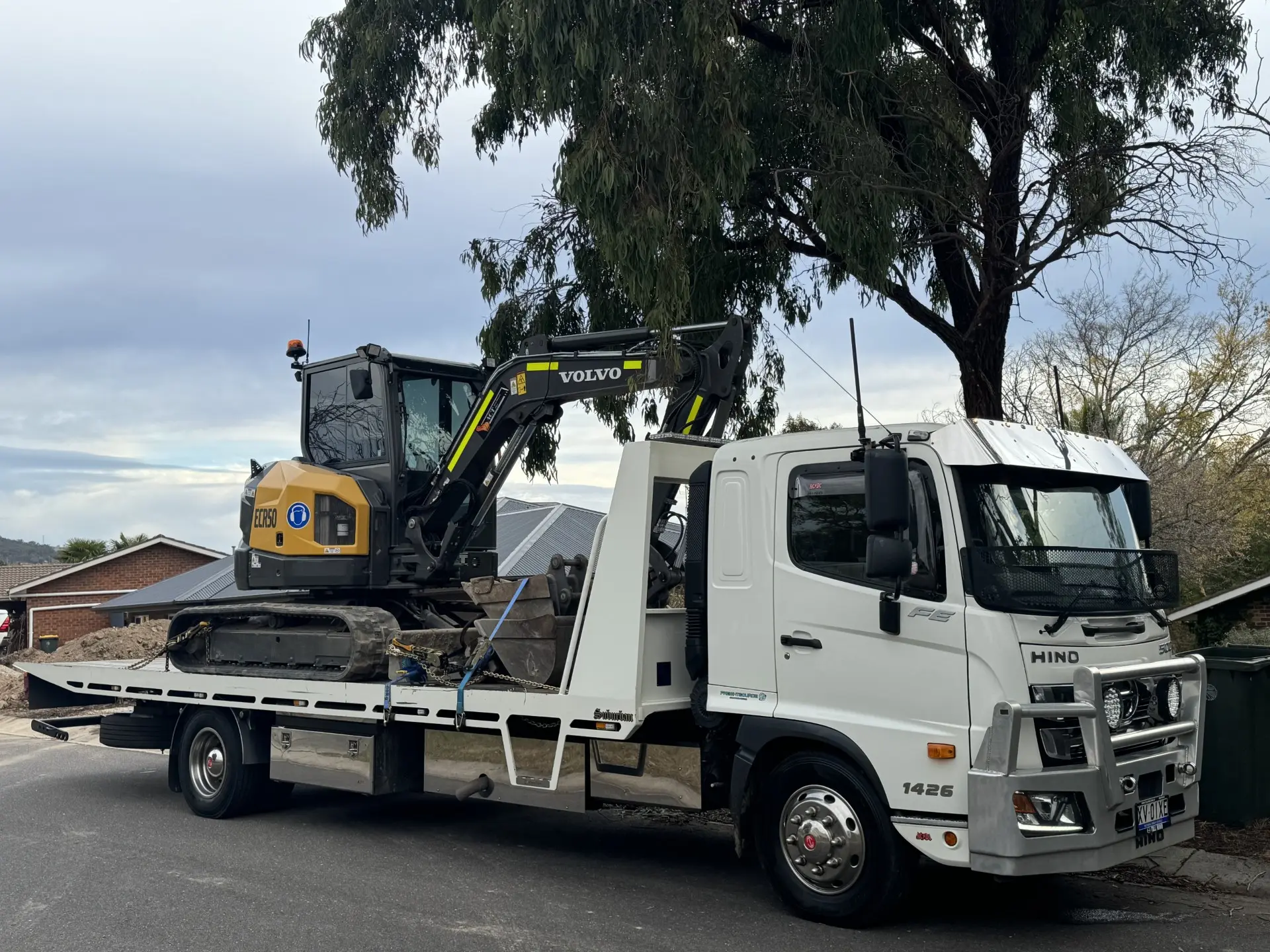 White truck carrying an excavator on a tree-lined road near Yass