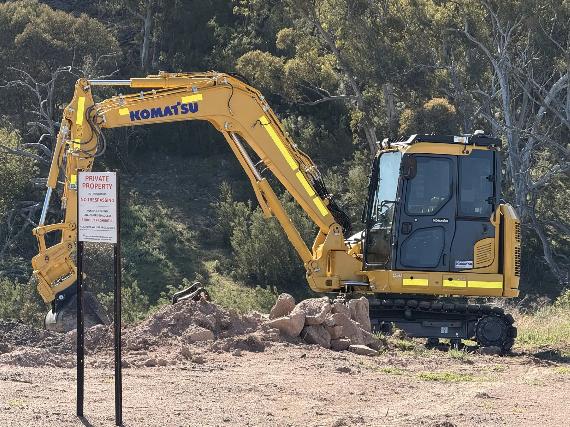 Yellow excavator digging at a fenced roadside site