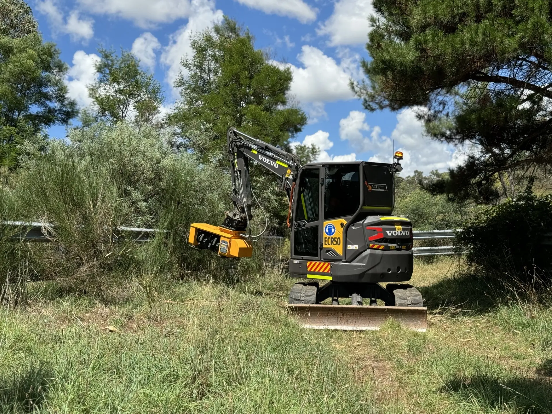 Excavator with a hydraulic hammer attachment working on a tree stump in bushland